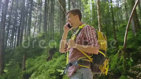 带着背包的年轻人在树林里打电话早晨的阳光透过树枝照耀视频的预览图