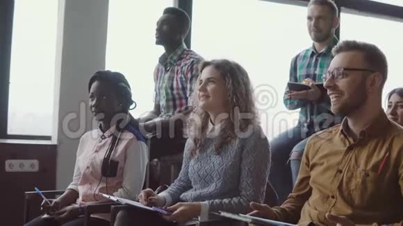 快乐的年轻团队坐在阁楼办公室参加商业研讨会混合种族的人一起做笔记一起笑视频的预览图