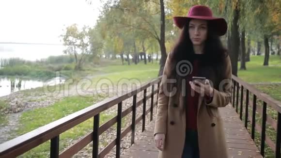 秋天公园里微笑的女人在电话里发短信视频的预览图