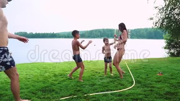 母亲带着父亲和两个孩子在草坪上玩耍倒着水笑着在操场上玩视频的预览图