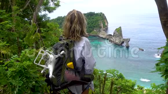 女人站在高高的悬崖上看着小岩石小岛努萨佩尼达岛的阿图海滩视频的预览图