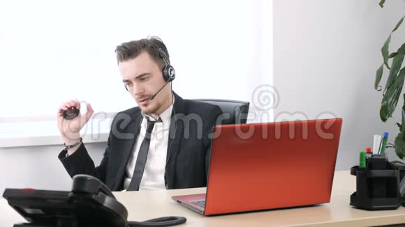 在办公室里工作穿西装的男人一边捏着扩手机一边坐在办公室里用耳机说话视频的预览图