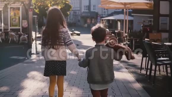 两个孩子一起走牵手慢动作后景在阳光明媚的日子里孩子们探索古老的镇街视频的预览图
