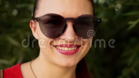 一位戴墨镜的黑发女郎的特写肖像女孩微笑着嘴唇是红色的口红在公园散步的女孩视频的预览图