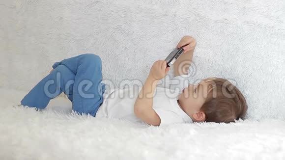 一个孩子躺在白色沙发上腿对腿玩智能手机视频的预览图