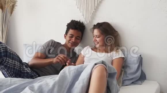 一对年轻可爱的多民族夫妇躺在床上聊天一个英俊的非洲男人牵着他的白人女友的手视频的预览图