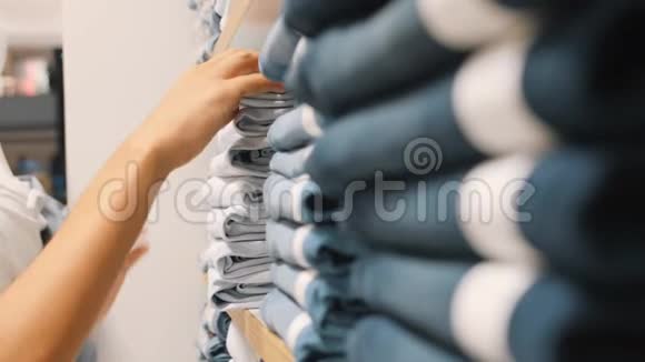 年轻的女人从服装店的书架上拿一条蓝色牛仔牛仔裤女性在购物时选择正确的裤子尺寸视频的预览图