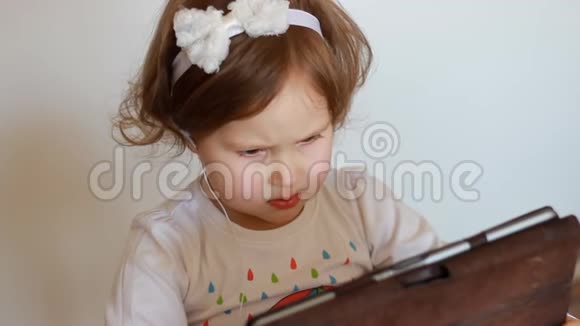 儿童耳机看屏幕监视器平板电脑一个小可爱的女孩看电视视频卡通或玩视频的预览图