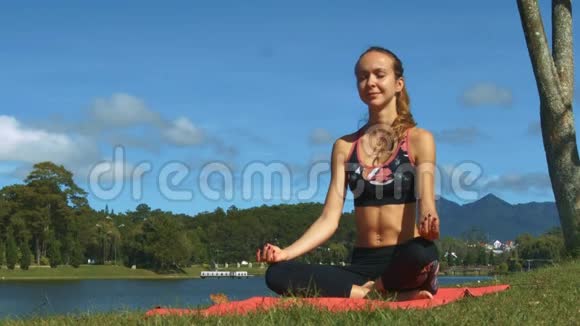 金发女孩在湖边的垫子上放松瑜伽姿势视频的预览图