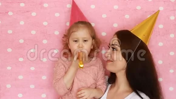 生日快乐母女俩戴着节日的帽子吹角笑嘻嘻的女人和孩子玩得开心视频的预览图