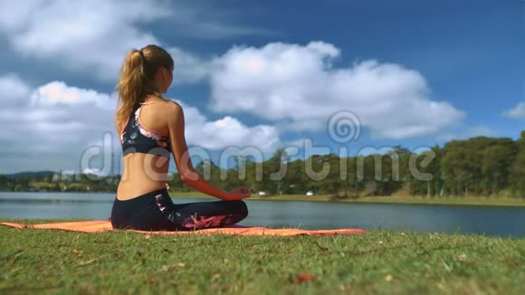 女人在天空下的湖岸上做瑜伽姿势视频的预览图