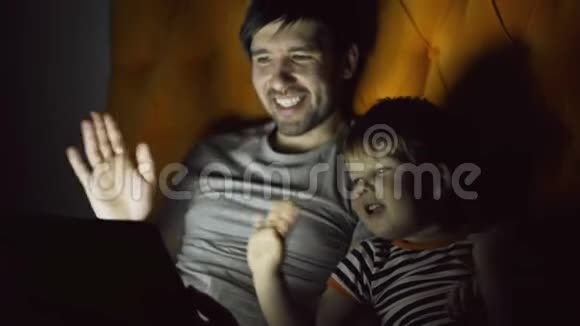 爱的父亲和他的小儿子在网上和祖父母用平板电脑聊天躺在床上视频的预览图