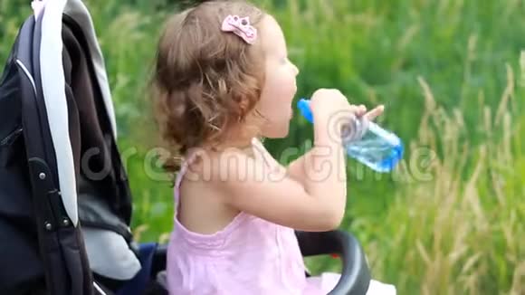 小女孩坐在婴儿车里从瓶子里喝水视频的预览图