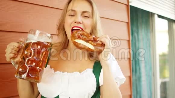 年轻的啤酒节女服务员穿着传统的巴伐利亚礼服端着大杯啤酒吃着椒盐卷饼视频的预览图