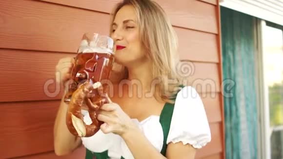 一个漂亮的女人喝啤酒吃椒盐脆饼巴伐利亚民族服装啤酒节女孩笑了视频的预览图