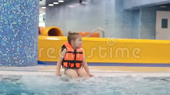泳池里穿着救生衣的小女孩坐在沸腾的蓝色水中正准备潜水视频的预览图