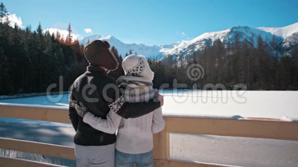 冬天年轻夫妇站在山湖附近欣赏兰斯卡普视频的预览图