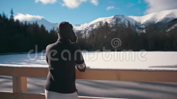 一个英俊的年轻人带着太阳光看冬天的山湖视频的预览图
