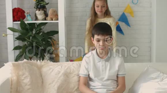 女孩闭上男孩眼睛而他坐在家里的沙发上视频的预览图
