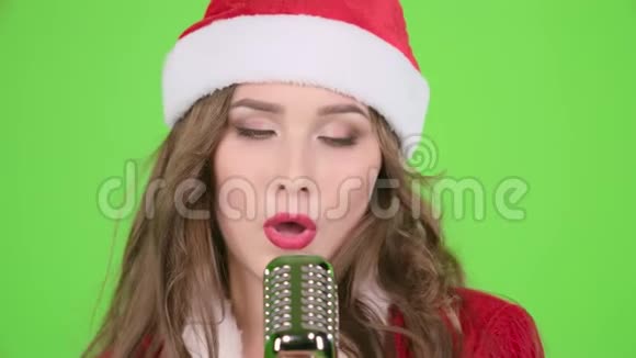 穿着圣诞老人套装的女孩用复古麦克风唱歌用充满活力的音乐跳舞绿色屏幕慢慢视频的预览图