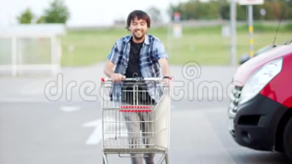 年轻开朗的家伙在停车场购物中心玩得很开心快乐有趣的家伙骑在购物车上顾客购物视频的预览图