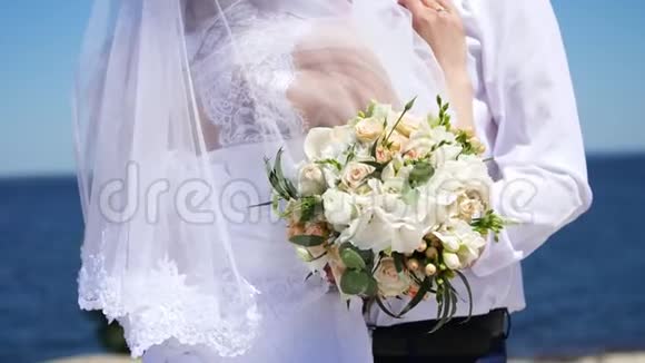 婚礼花束的特写新婚夫妇穿着婚纱拥抱在一起在背景中大海和天空视频的预览图