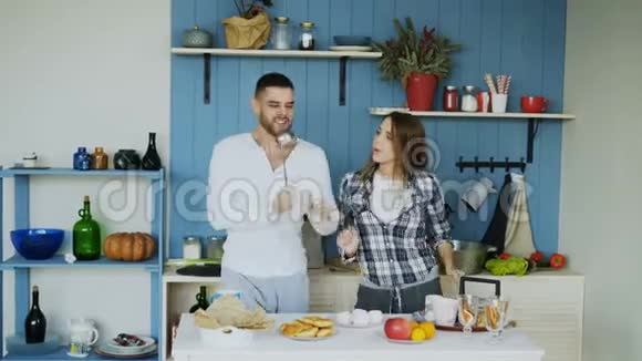 快乐的年轻夫妇在厨房里跳舞唱歌早上在家听音乐视频的预览图