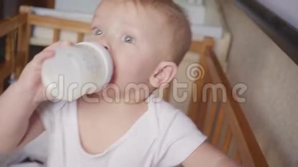 两岁的男孩在床上喝着塑料瓶里的牛奶视频的预览图