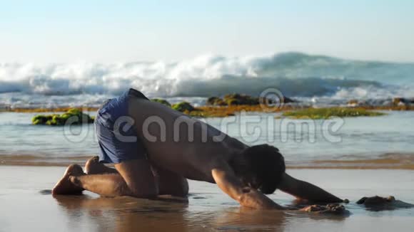穿蓝色短裤的肌肉体操运动员在海滩上练习瑜伽视频的预览图
