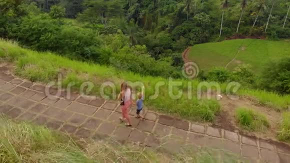 一名年轻女子和她的小儿子在艺术家步行坎布汉岭步行在乌布村的空中拍摄视频的预览图