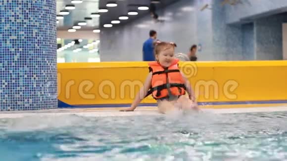 泳池里穿着救生衣的小女孩坐在沸腾的蓝色水中正准备潜水视频的预览图