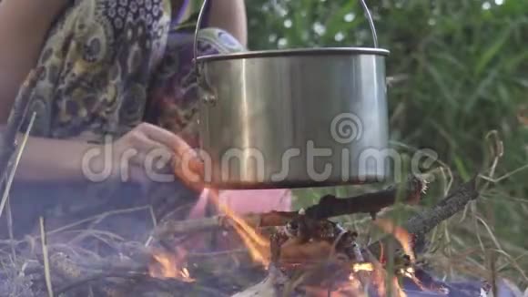 女人在森林里生火做饭锅煮饭用的锅挂在火棒上她在Touri下面打柴视频的预览图