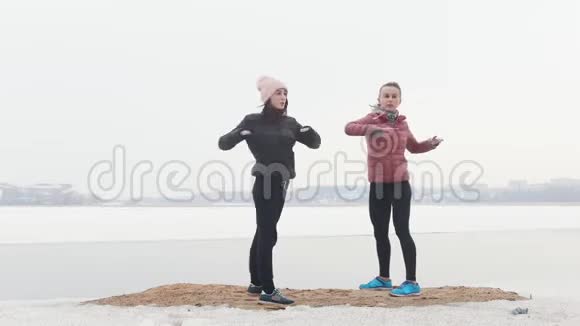 两个苗条的女人在雪地海滩上训练热身运动视频的预览图
