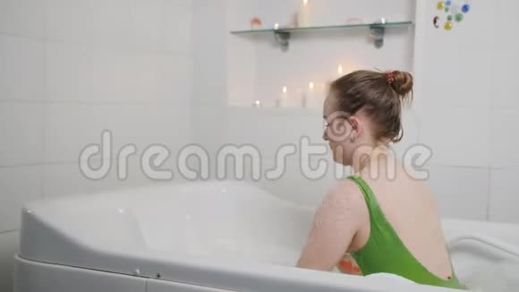 穿着泳衣的快乐女孩在一次放松的水上按摩和慢动作中用泡沫泡澡视频的预览图