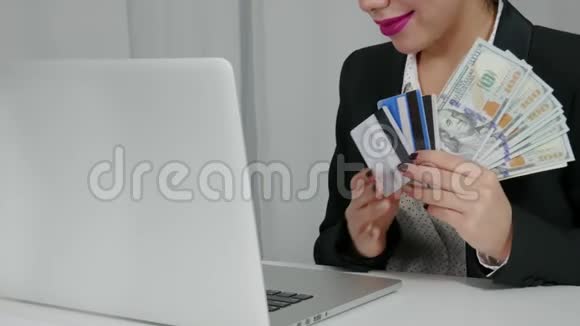 幸福的女人拿着美元和信用卡靠近她的笔记本电脑视频的预览图
