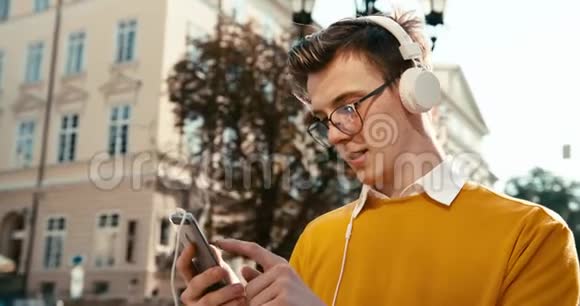 戴眼镜的英俊的金发少年通过耳机听音乐浏览聊天和发短信视频的预览图
