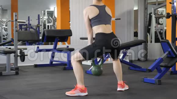 年轻漂亮的运动女孩在健身房里用水壶铃做加权蹲后侧视60fps视频的预览图