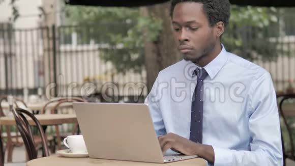 非洲商人坐在户外咖啡厅时一边工作一边用笔记本电脑视频的预览图