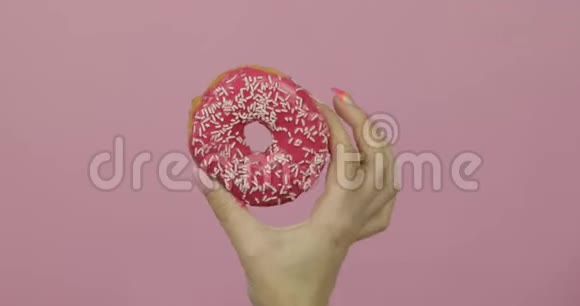 女人手里拿着红色的美味的洒在粉红色背景上的甜甜圈视频的预览图