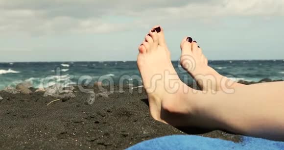 女子双脚特写在黑色沙滩上放松视频的预览图
