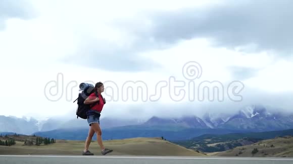年轻的旅游妇女带着背包走在山路上那里有雪山视频的预览图