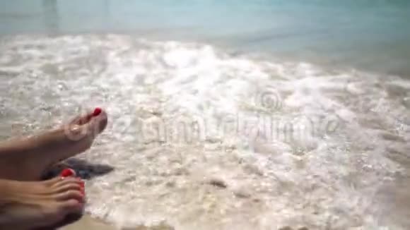 海浪冲刷着晒黑的雌性腿美丽的年轻女子在暑假期间在海岸放松女孩的脚躺在视频的预览图