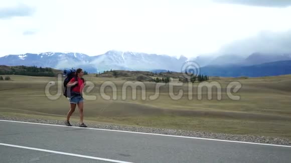 旅行者女孩带着背包走在山路的一侧背景中有雪山视频的预览图