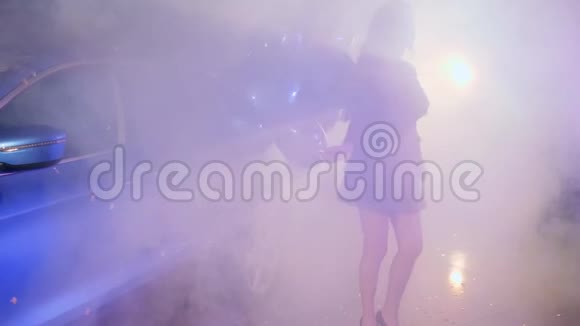 丰富的生活时髦的女性带着蓝色的气球在雾中的停车场跳舞视频的预览图