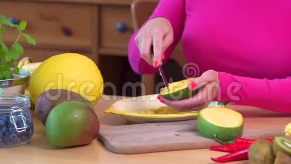 穿着粉红色上衣的女人在桌子上切一个多汁的黄色芒果视频的预览图