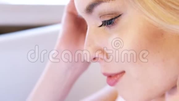 一个漂亮的金发女人有着深蓝色的眼睛和完美的妆容坐在浴室里思考着视频的预览图
