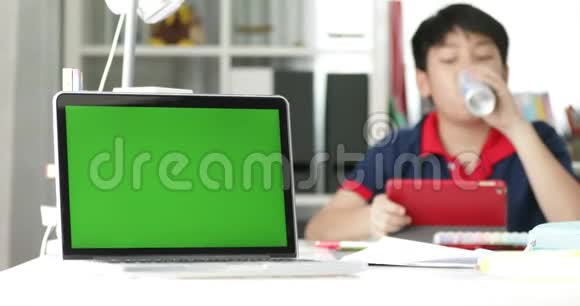 笔记本电脑上的绿色屏幕和背景平板电脑上的亚洲男孩视频的预览图