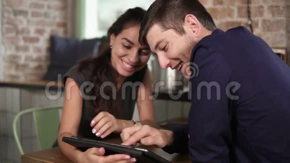 浪漫的年轻夫妇在咖啡店里用平板电脑女人手指着触摸屏视频的预览图