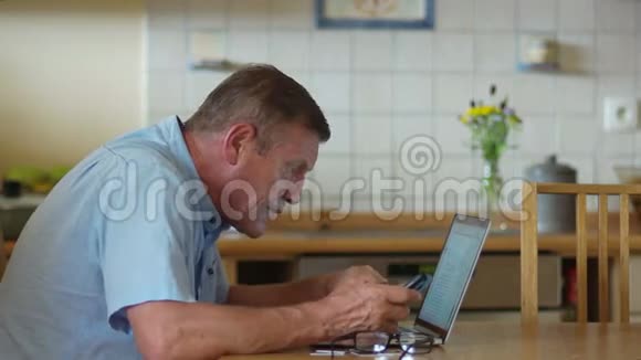 退休年龄的人使用笔记本电脑和电话他仔细地看着电脑屏幕眯着眼睛戴着眼镜视频的预览图