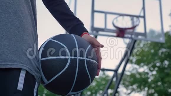 女性手拿篮球站在公园背景篮圈白天的近镜头视频的预览图